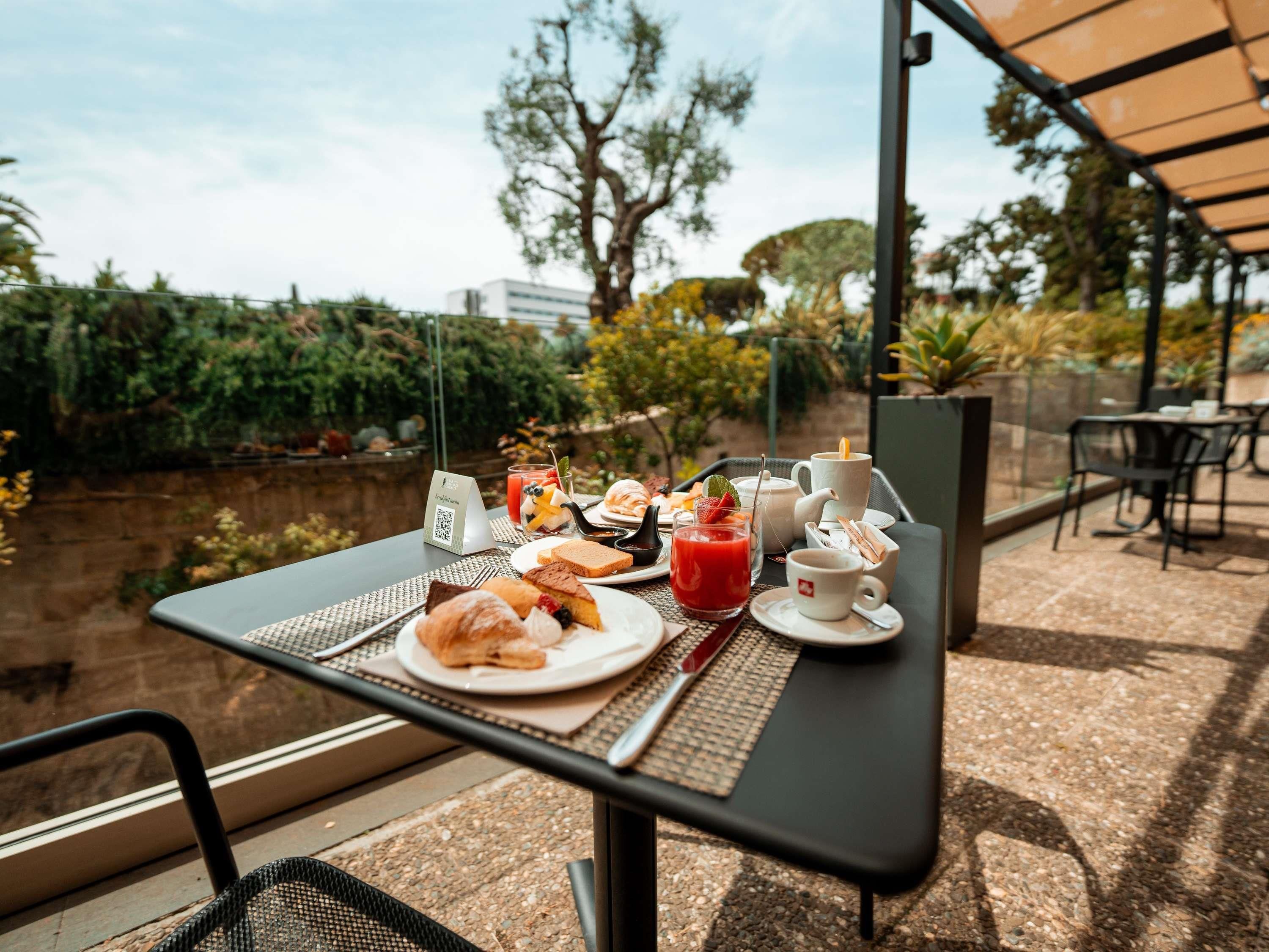 An outdoor dining area with a table set for breakfast, including croissants, a glass of red juice, and a cup of coffee.