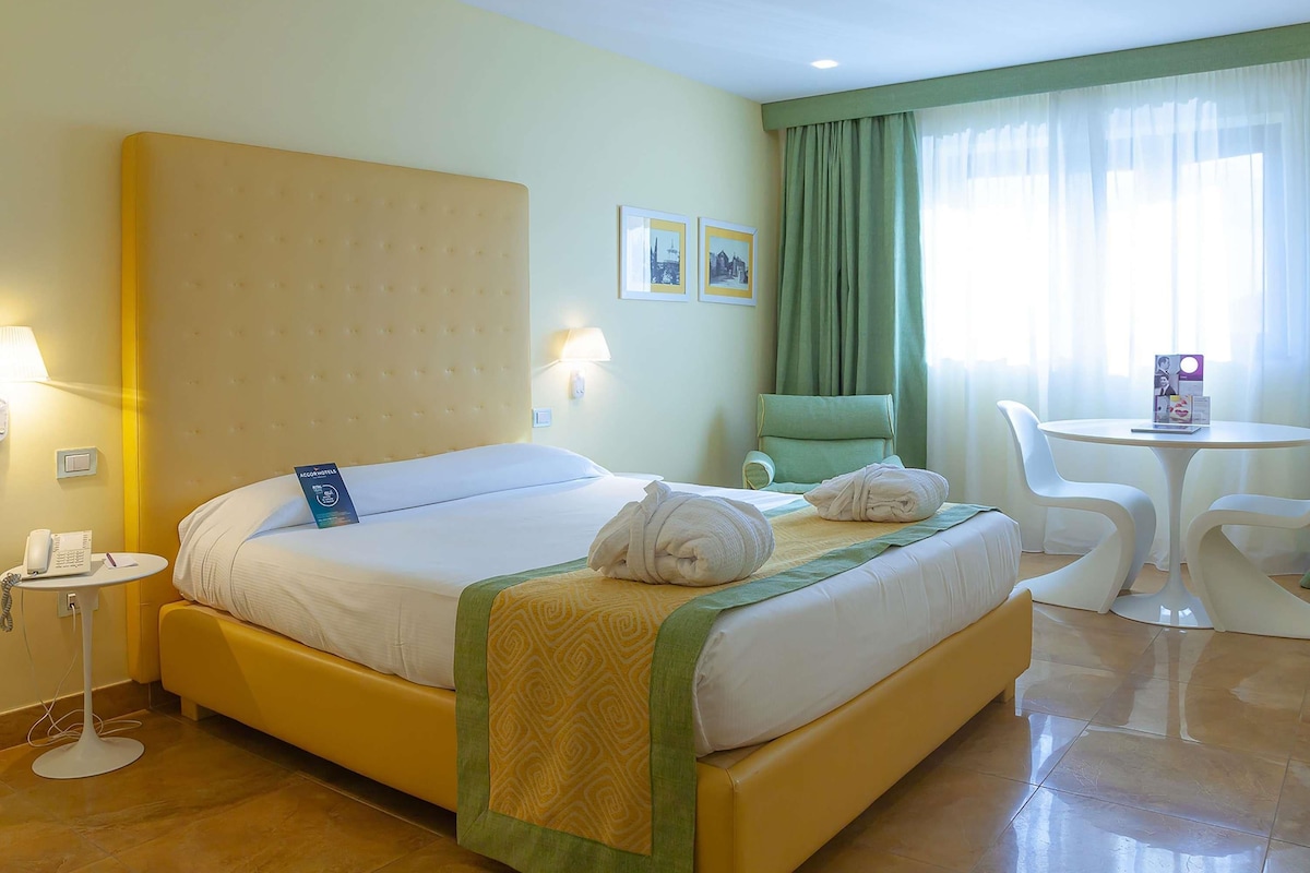 A hotel room with a bed, a chair, a small table, and a lamp.