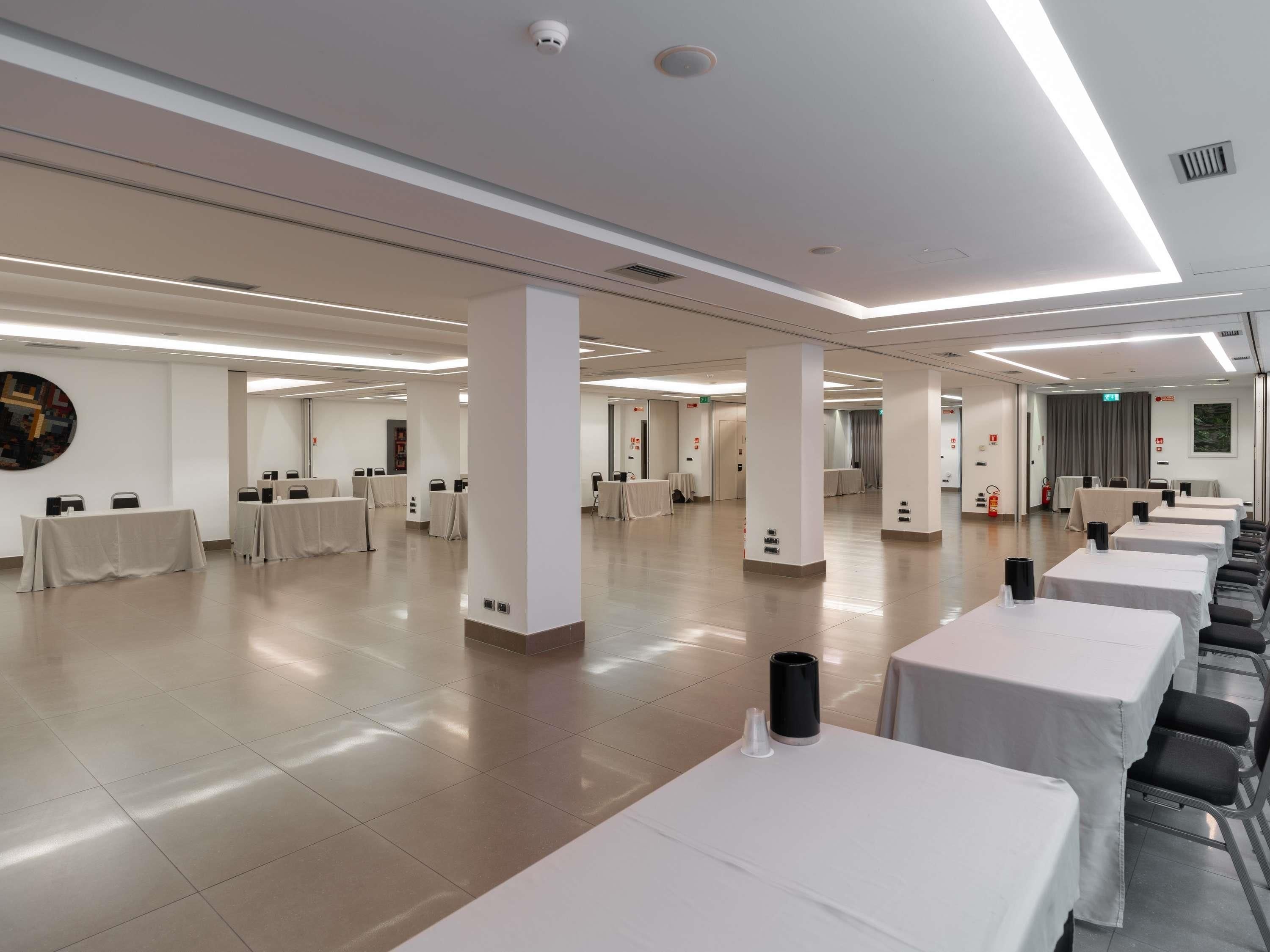 Une salle de conférence spacieuse, dotée de plusieurs tables et chaises, de murs blancs et d’un éclairage au plafond.