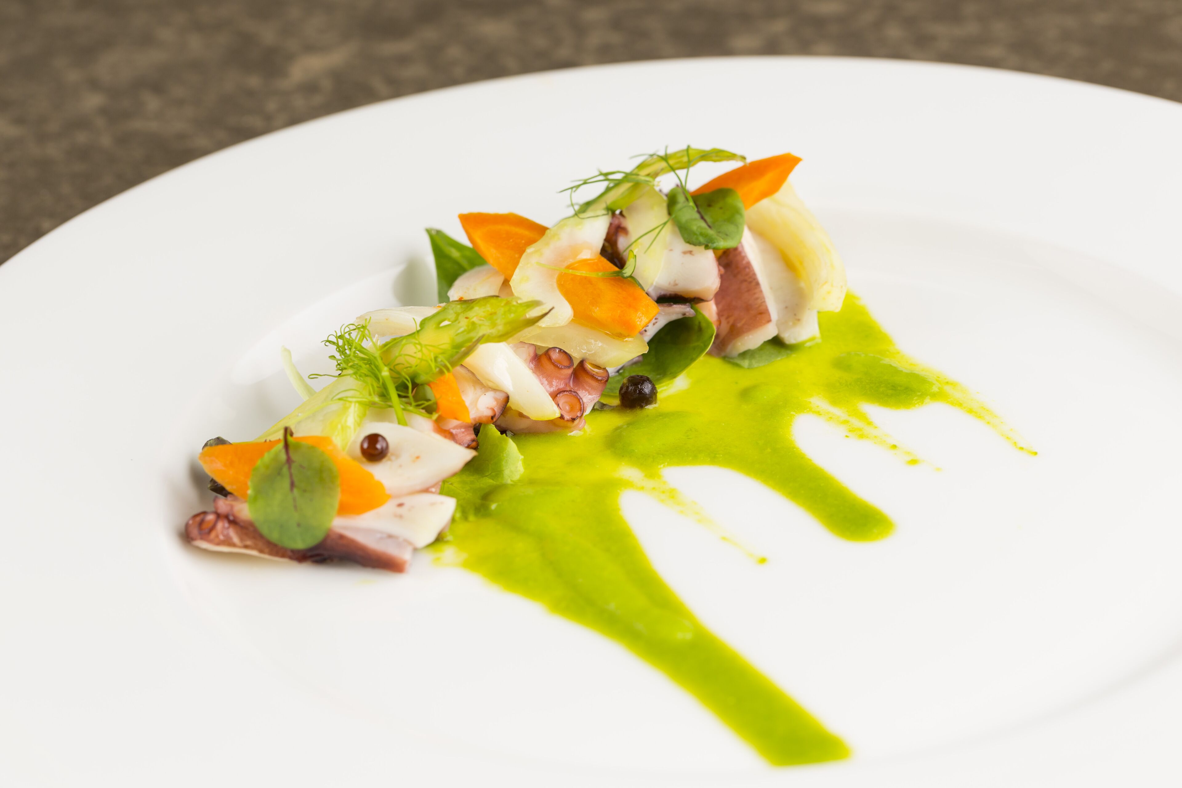 Un plato blanco con un plato de mariscos, adornado con hierbas y salsa verde.