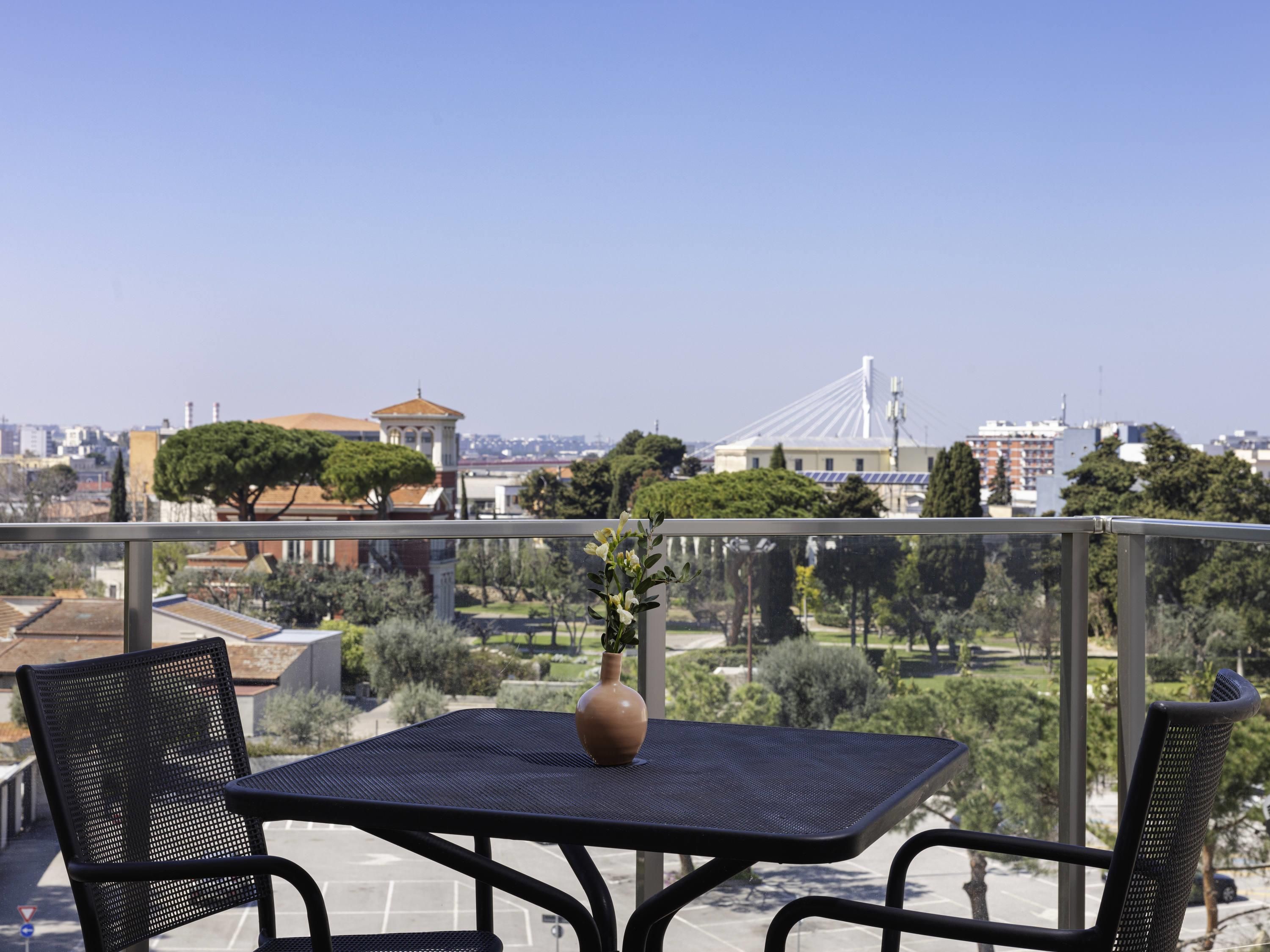 Un balcone con tavolo e sedie, un vaso con fiori e vista sulla città.