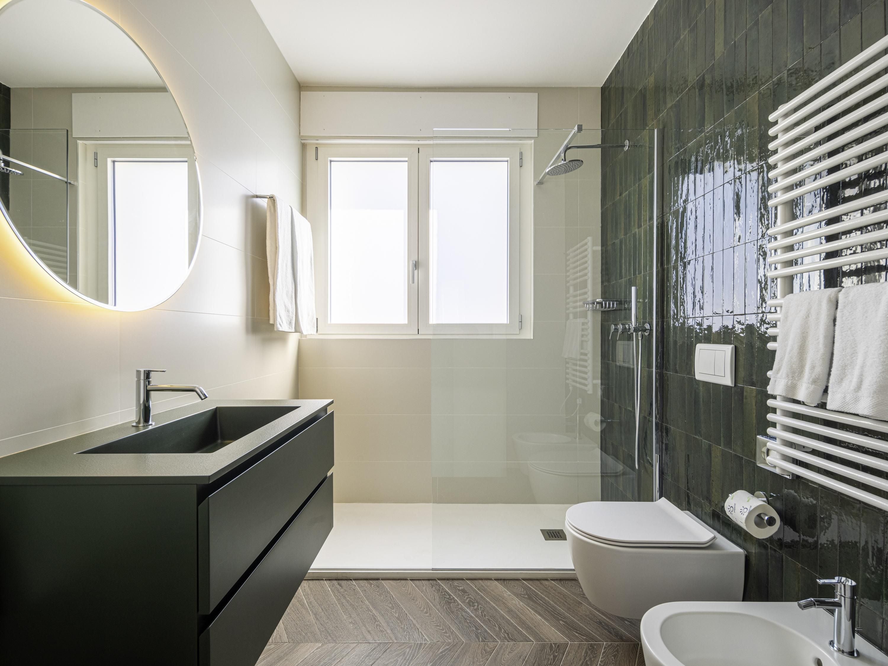 Un baño moderno con un espejo grande, un lavamanos, un inodoro y una zona de ducha.