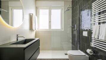 Un baño moderno con un espejo grande, un lavamanos, un inodoro y una zona de ducha.