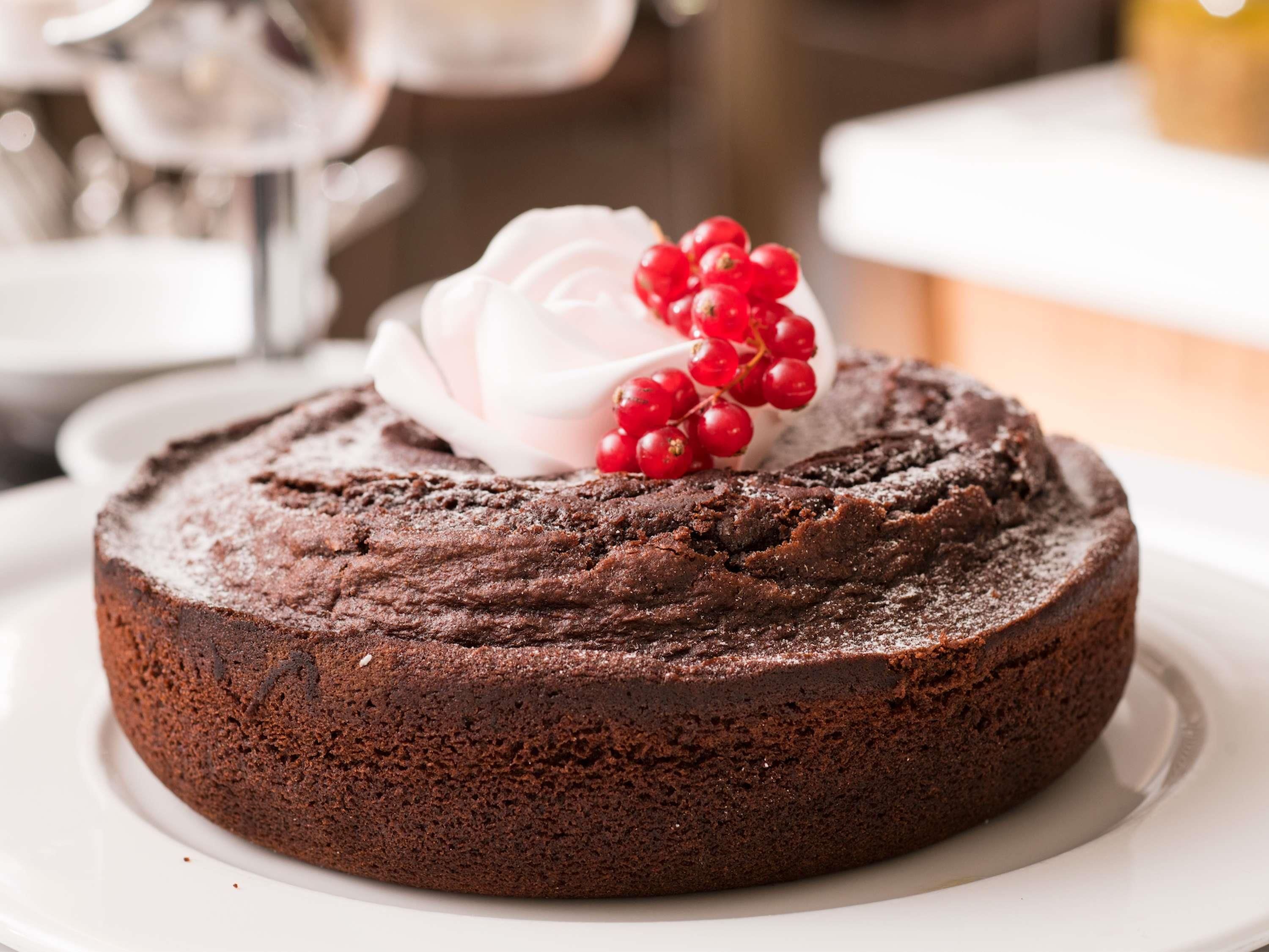 A round chocolate cake with a dusting of powdered sugar and a dollop of whipped cream on top, garnished with red berries.
