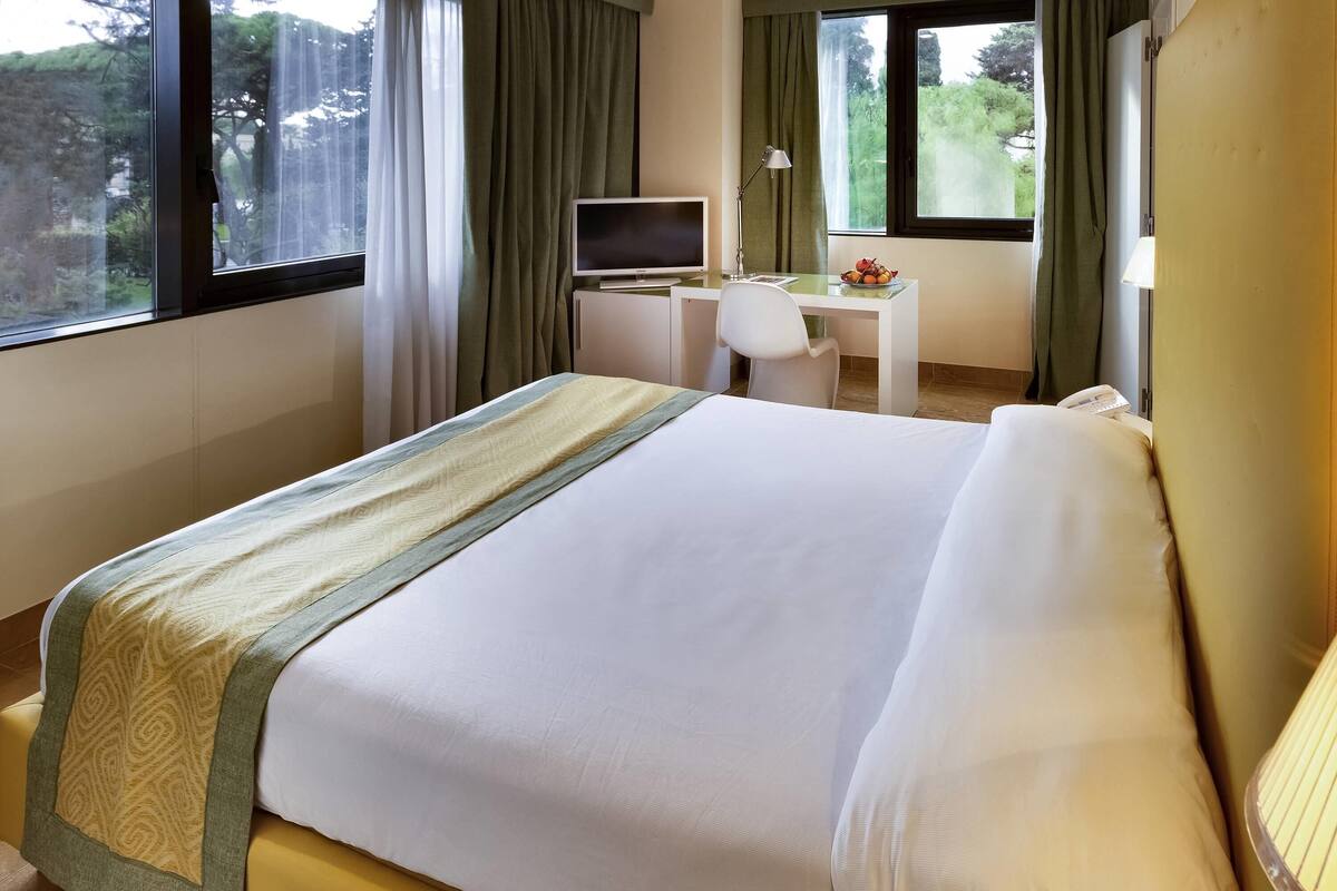 Una camera d'albergo con un letto, una scrivania con un computer e una finestra con tende.