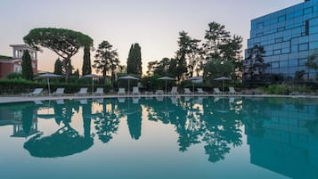 Ein Schwimmbecken mit Liegestühlen und Sonnenschirmen, umgeben von Bäumen und einem modernen Gebäude.