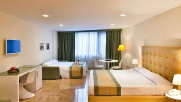 Ein Hotelzimmer mit Bett, Schreibtisch, Stuhl, kleinem Tisch, Fernseher und einem Fenster mit Vorhängen.