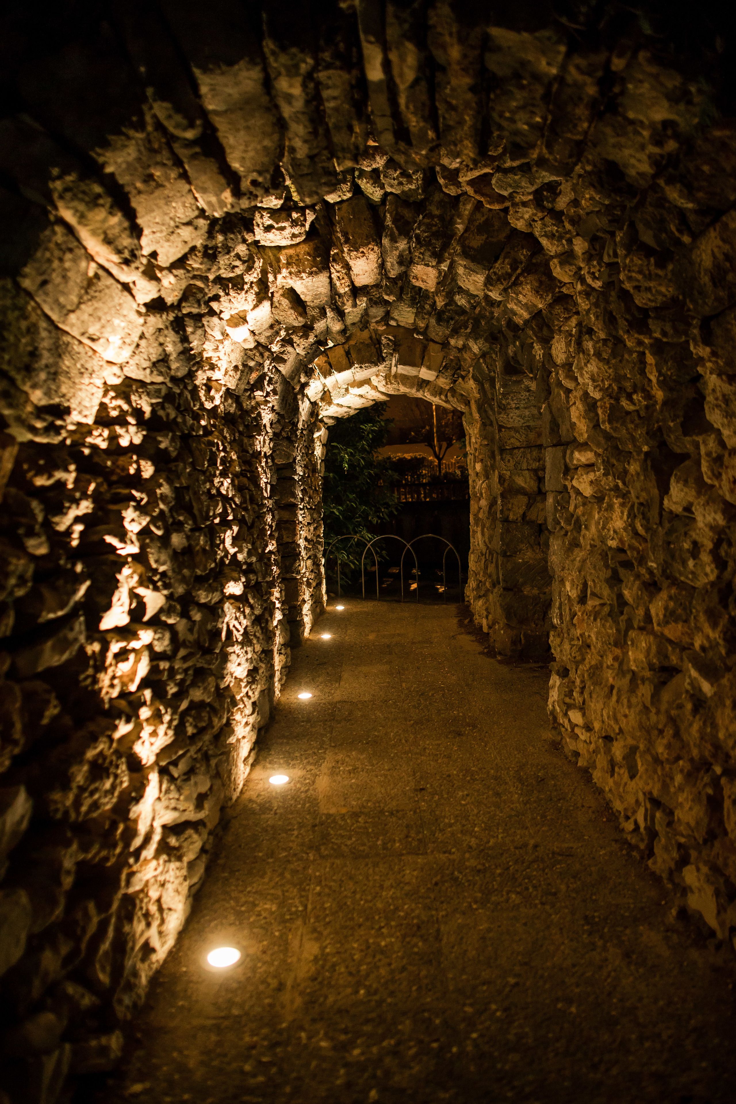 A stone tunnel with a narrow pathway and a metal railing in the distance.