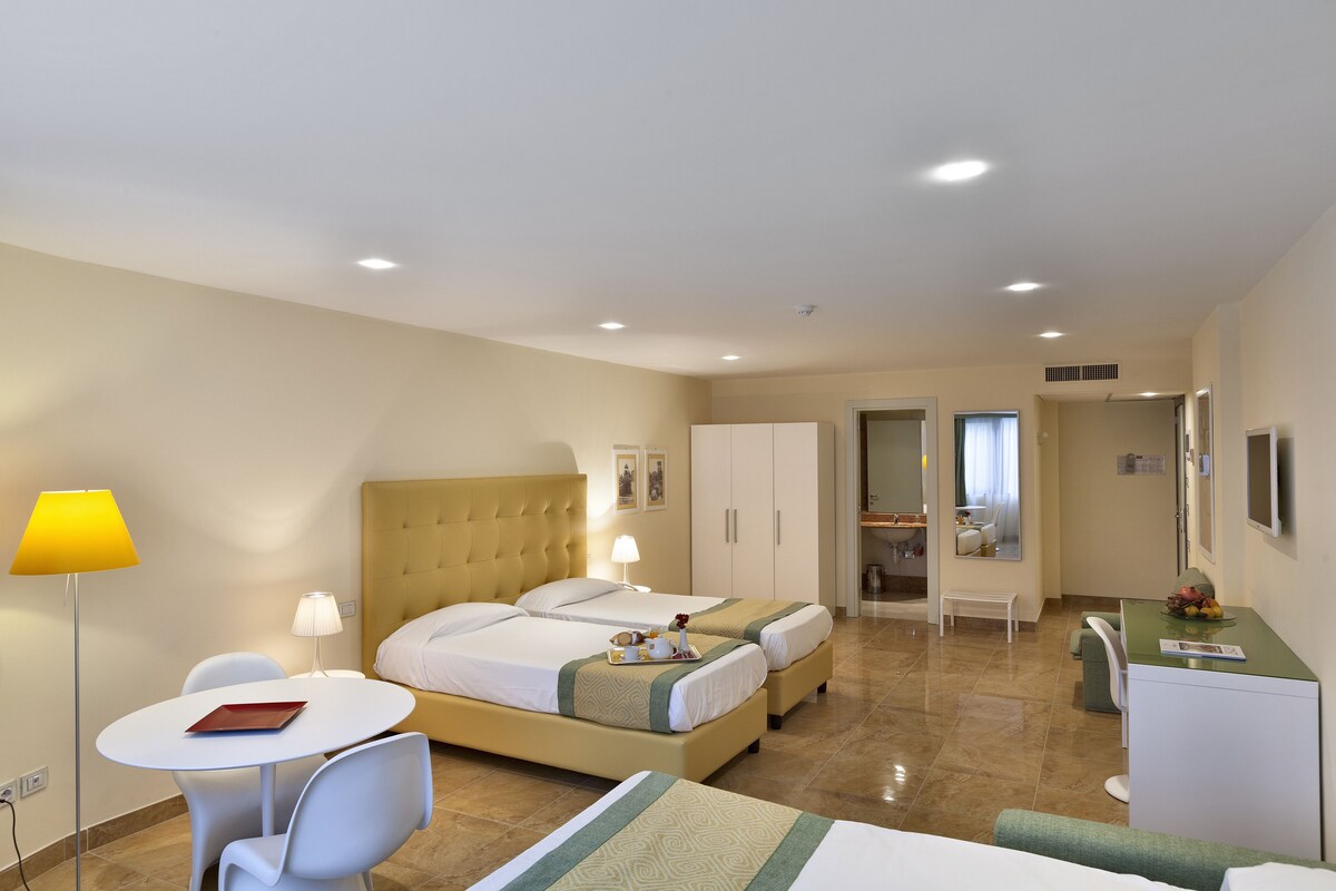 A hotel room with a bed, two bedside tables, a desk, a chair, and a lamp.