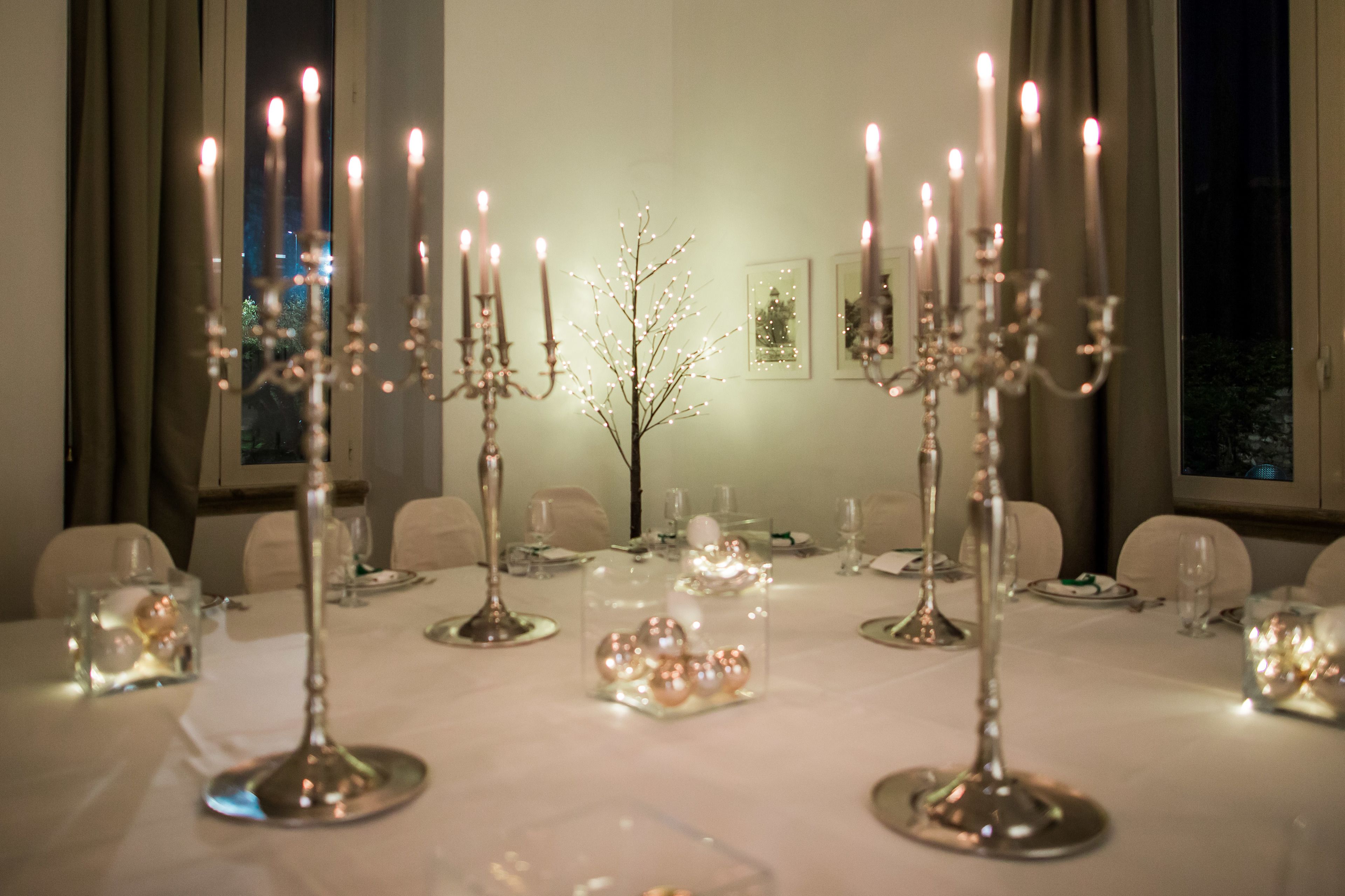 Una mesa de comedor dispuesta para una comida, con candelabros, portavelas de cristal y un florero con flores.