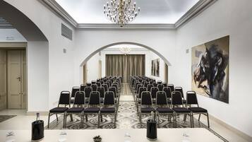 Un salón de conferencias con filas de sillas, una larga mesa y un candelabro.