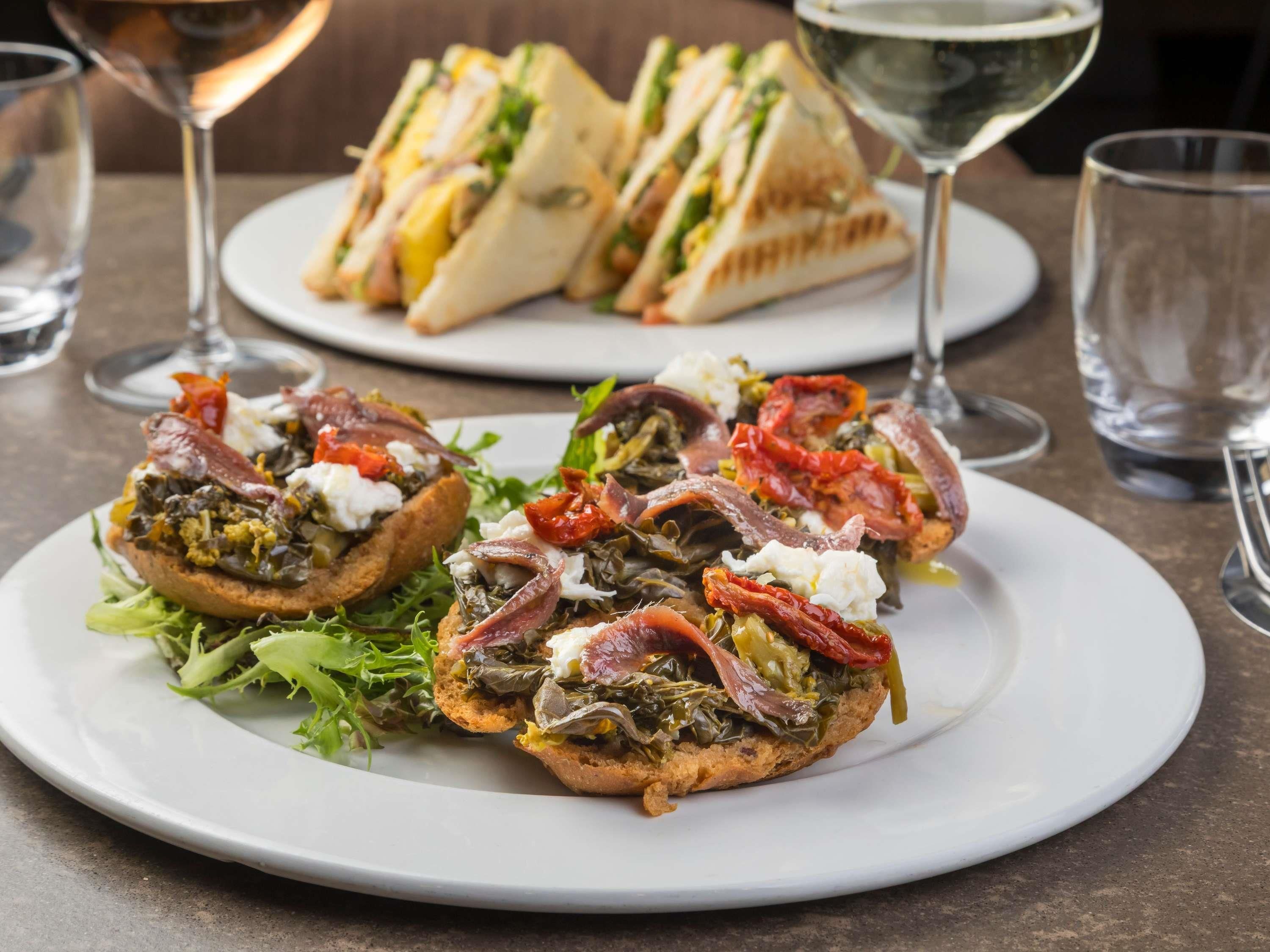 A plate of bruschetta topped with greens, tomatoes, and cured meats, accompanied by a glass of white wine.