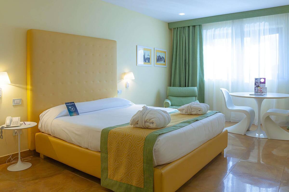 A hotel room with a bed, a chair, a small table, and a lamp.