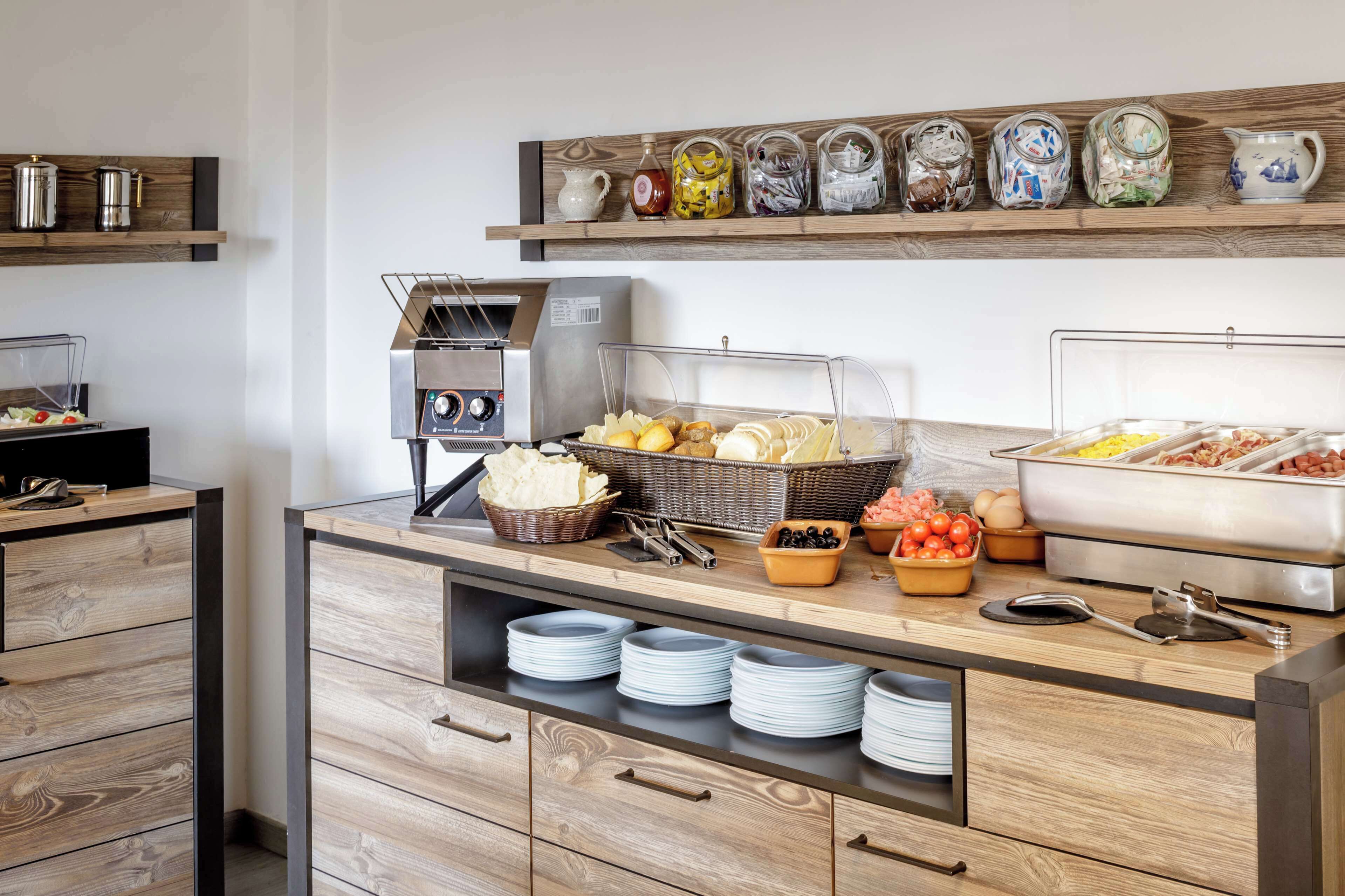 A buffet setup with various food items, a coffee machine, and decorative jars on shelves.