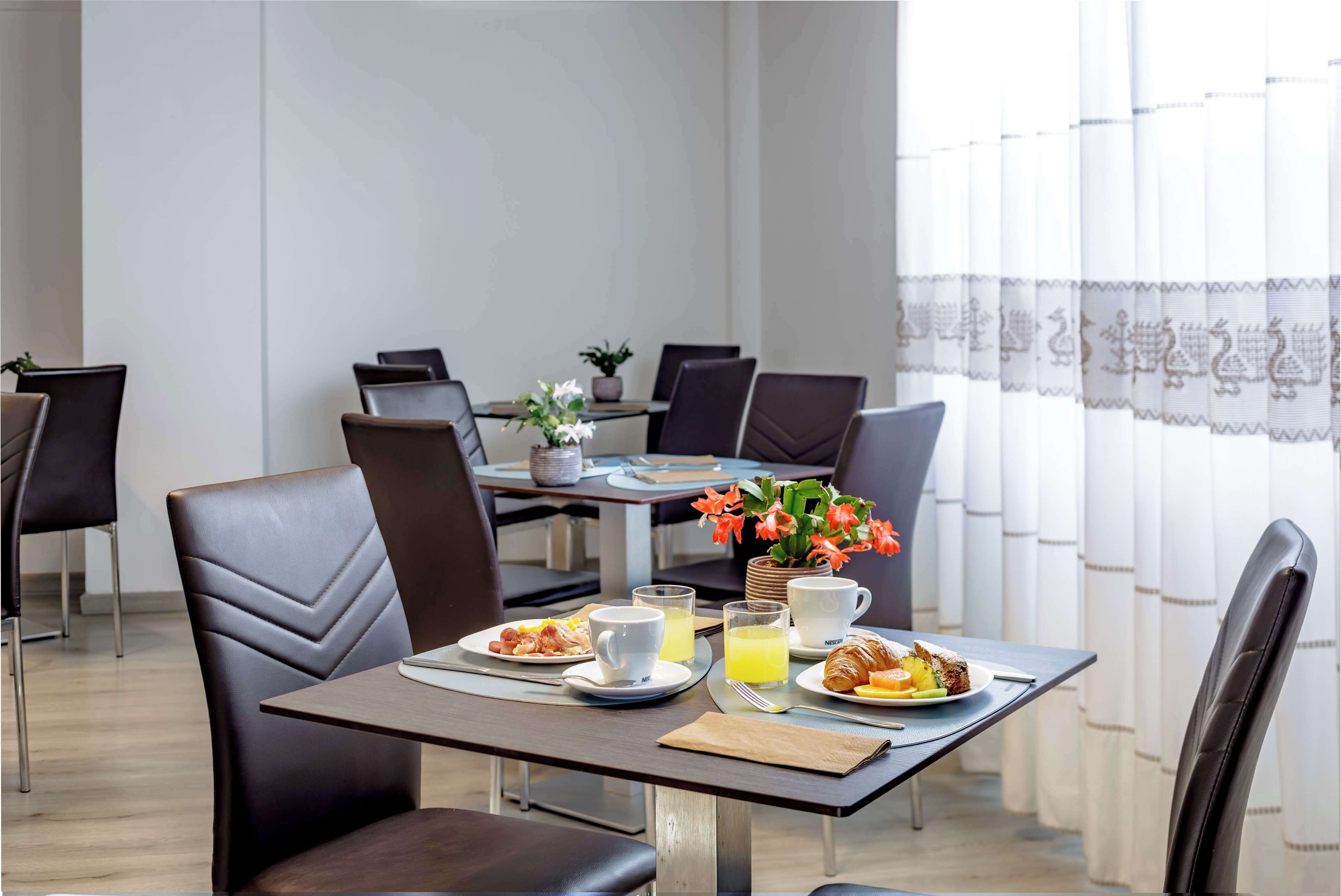A dining area with a table set for breakfast, including plates of food, cups, and a vase of flowers.