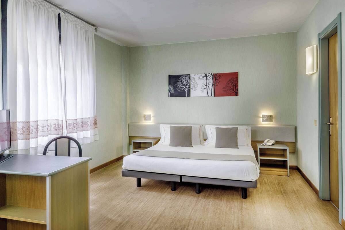 Et hotelværelse med seng, sengeborde, et skrivebord og en stol.