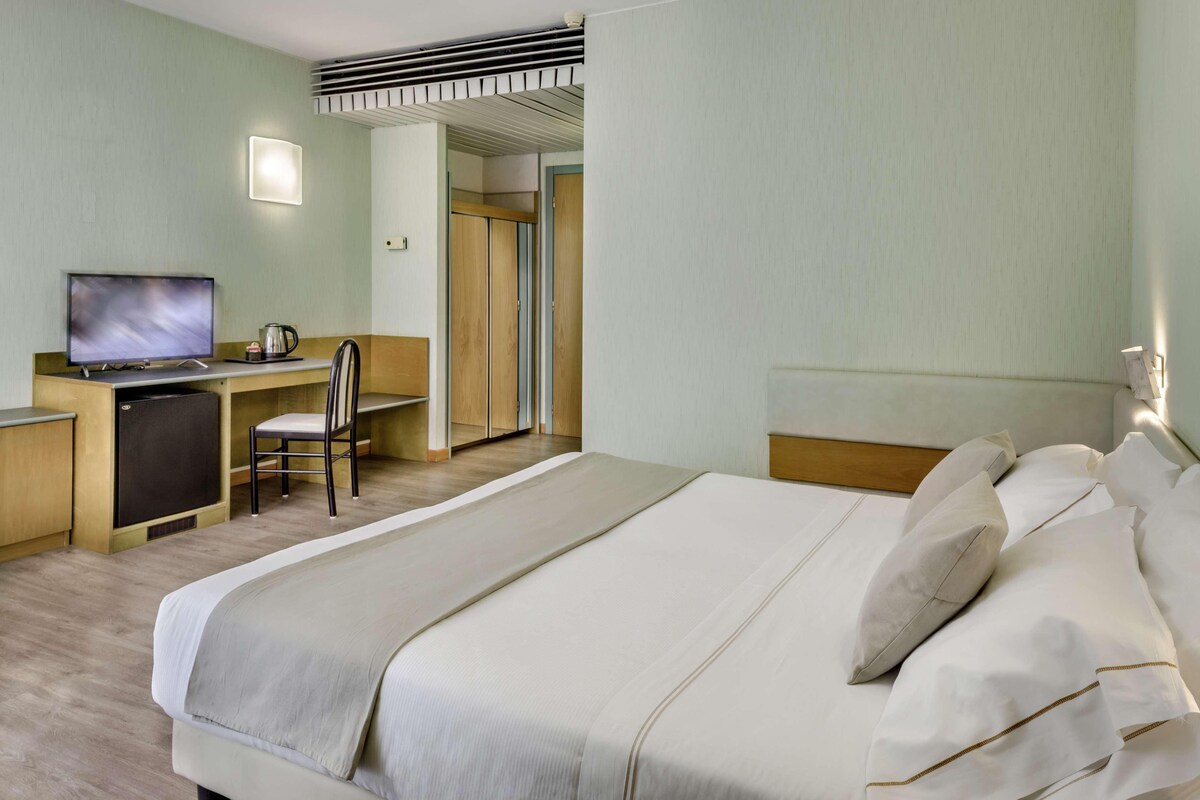 Une chambre d’hôtel comprenant un lit, un bureau avec une télévision, une chaise et une armoire.