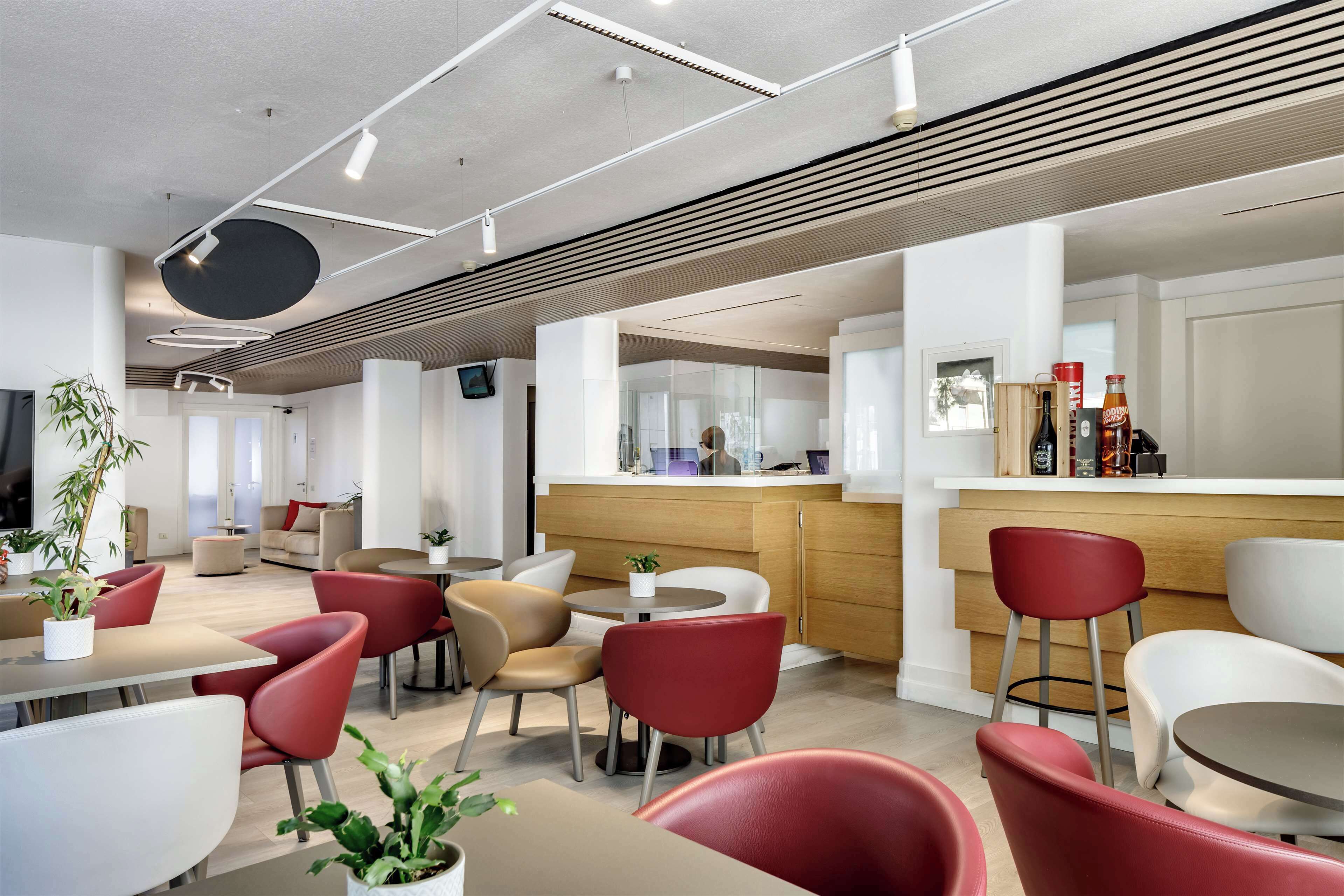 A modern dining area with red and beige chairs, a wooden counter, and a large mirror.
