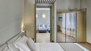 Habitación de hotel con una cama grande, un área de estar independiente y un balcón al que se accede por una puerta corrediza.
