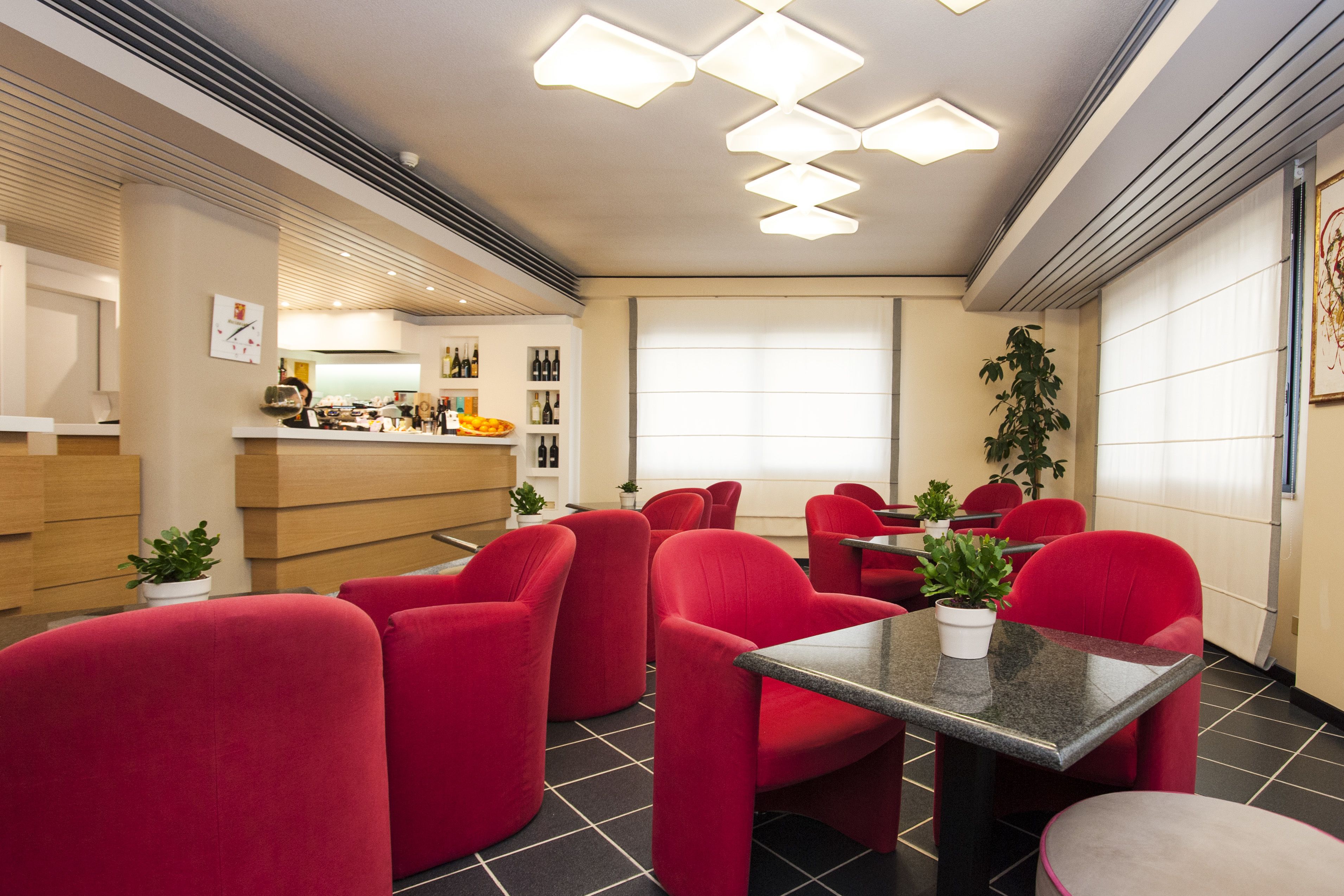 A modern restaurant with red chairs and tables, a visible kitchen area, and a large window with blinds.