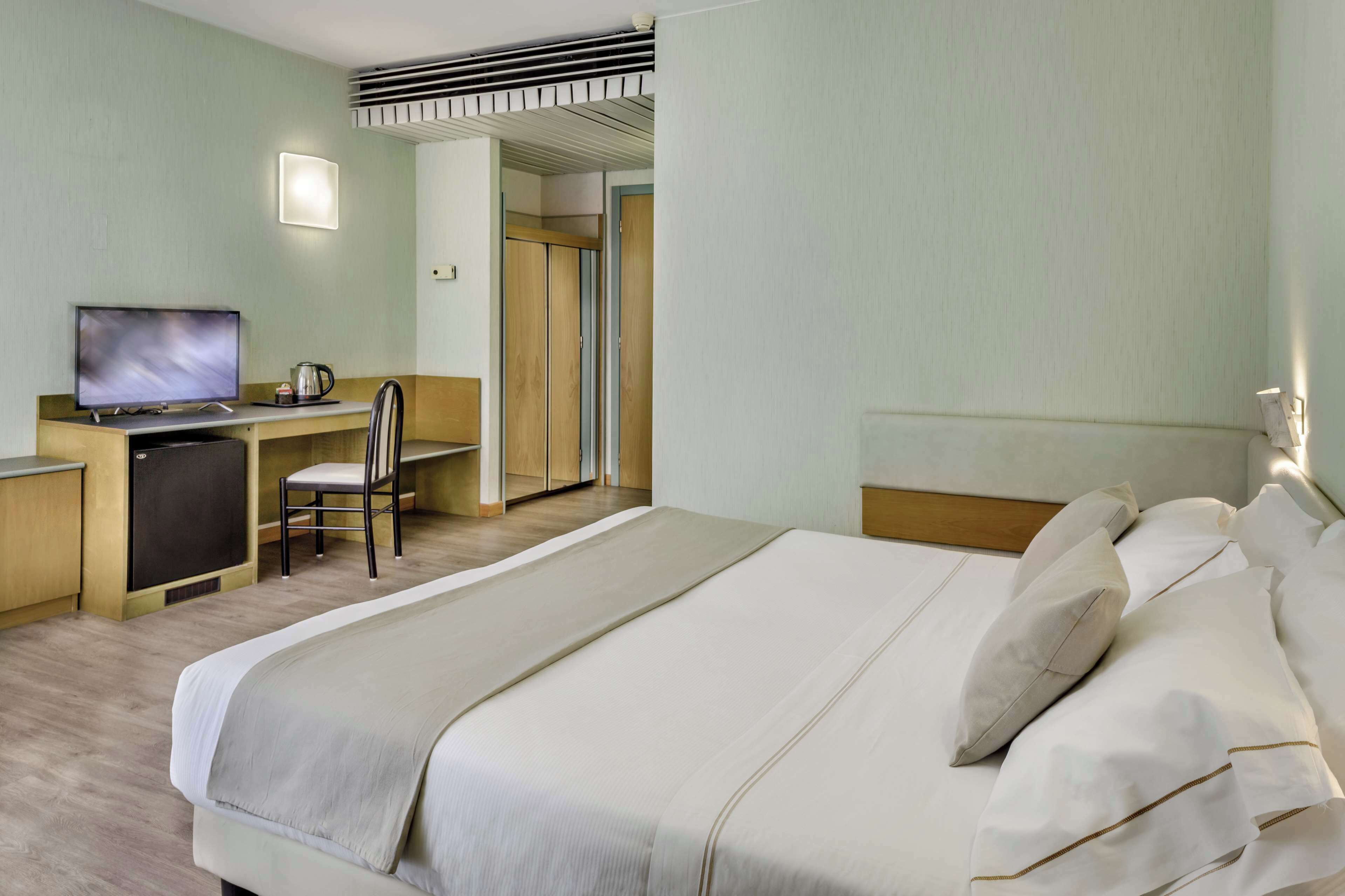 A hotel room with a bed, a desk with a television, a chair, and a wardrobe.