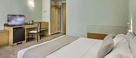 A hotel room with a bed, a desk with a television, a chair, and a wardrobe.