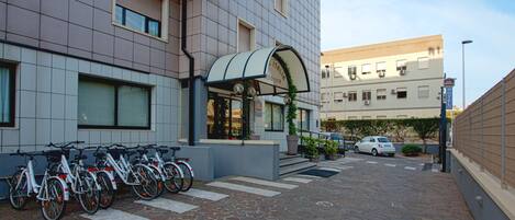 A hotel entrance with a row of bicycles parked outside, a car parked in the driveway, and a clear sky.