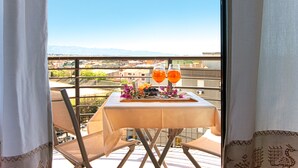 Un balcón con una mesa preparada para dos personas, que incluye una botella de zumo de naranja, una copa de vino y un plato de aceitunas.