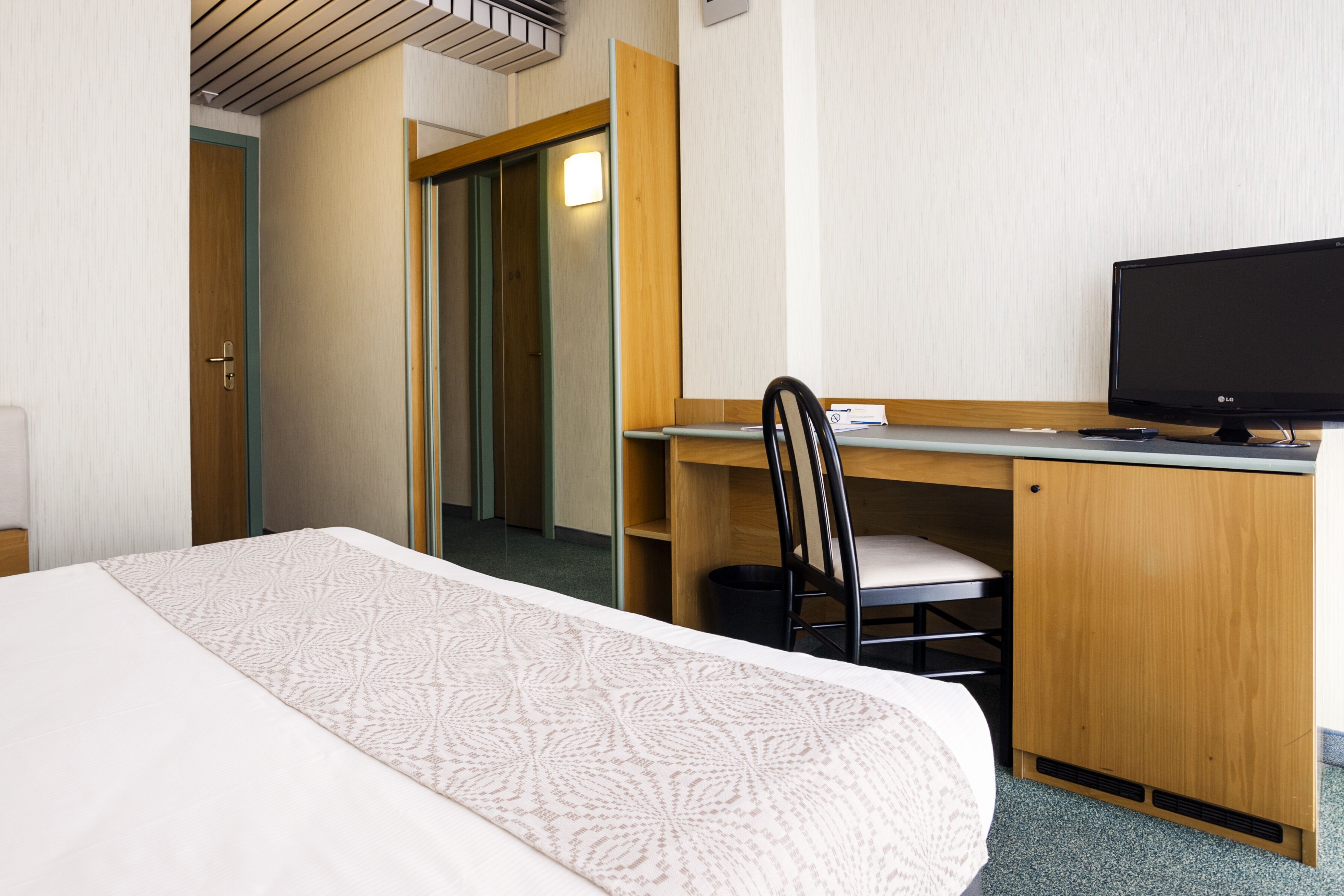 A hotel room with a bed, a desk with a computer, a chair, and a wardrobe.