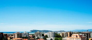 Un paisaje costero con edificios de apartamentos modernos, cielo azul despejado y una cadena montañosa distante.