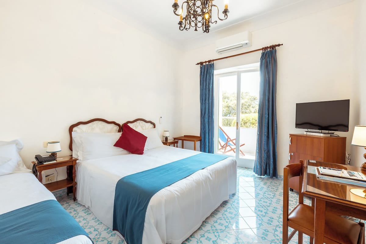 A hotel room with two beds, a television, a desk with a chair, and a balcony with a view.