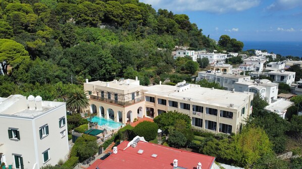 Zona residencial con un edificio grande que tiene piscina, rodeada de vegetación exuberante y vista al mar.