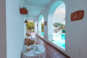 Comedor con mesas dispuestas para el servicio, con vistas a una piscina y a un paisaje de colinas.