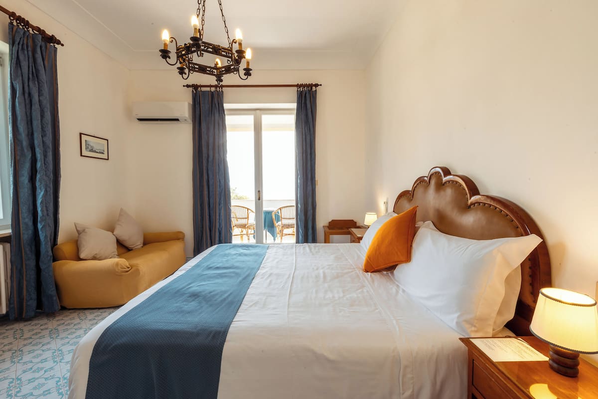 A hotel room with a large bed, a sofa, a chandelier, and a view of the outside.
