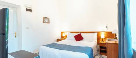 A hotel room with a bed, bedside tables, a desk, a TV, and a bathroom.