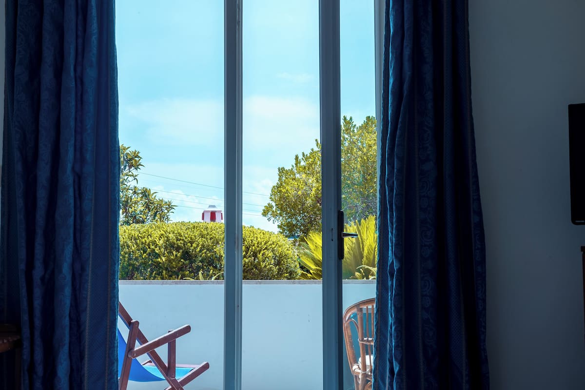 A room with a large sliding glass door, a wicker chair, and a view of greenery and a building outside.