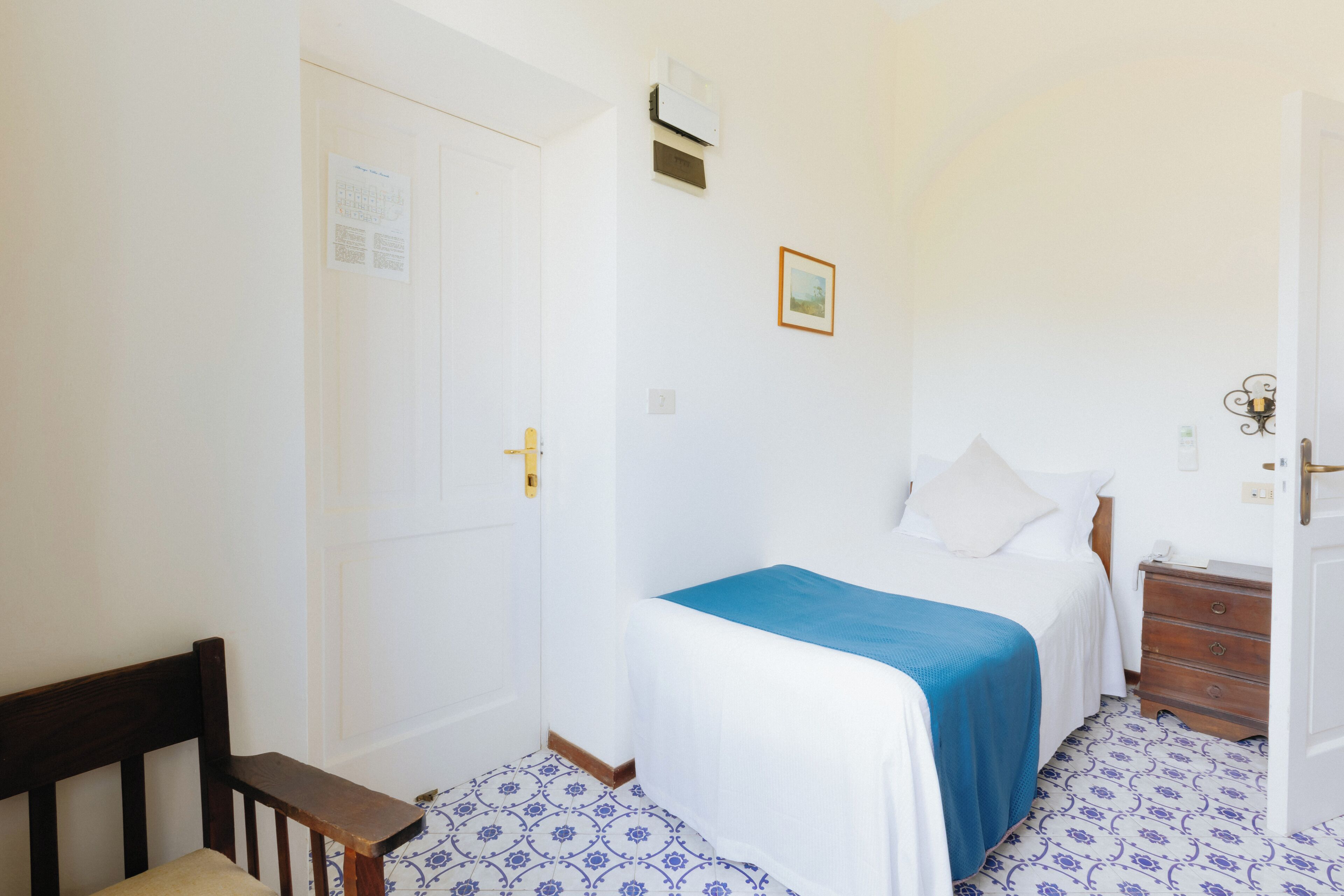 Une chambre à coucher avec un lit, une chaise en bois, une commode et des carreaux de sol à motifs.