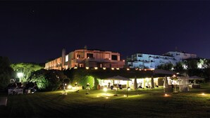 A nighttime outdoor event with illuminated tables and chairs, a gazebo, and buildings in the background. - Hotel Della Baia (Cellole)