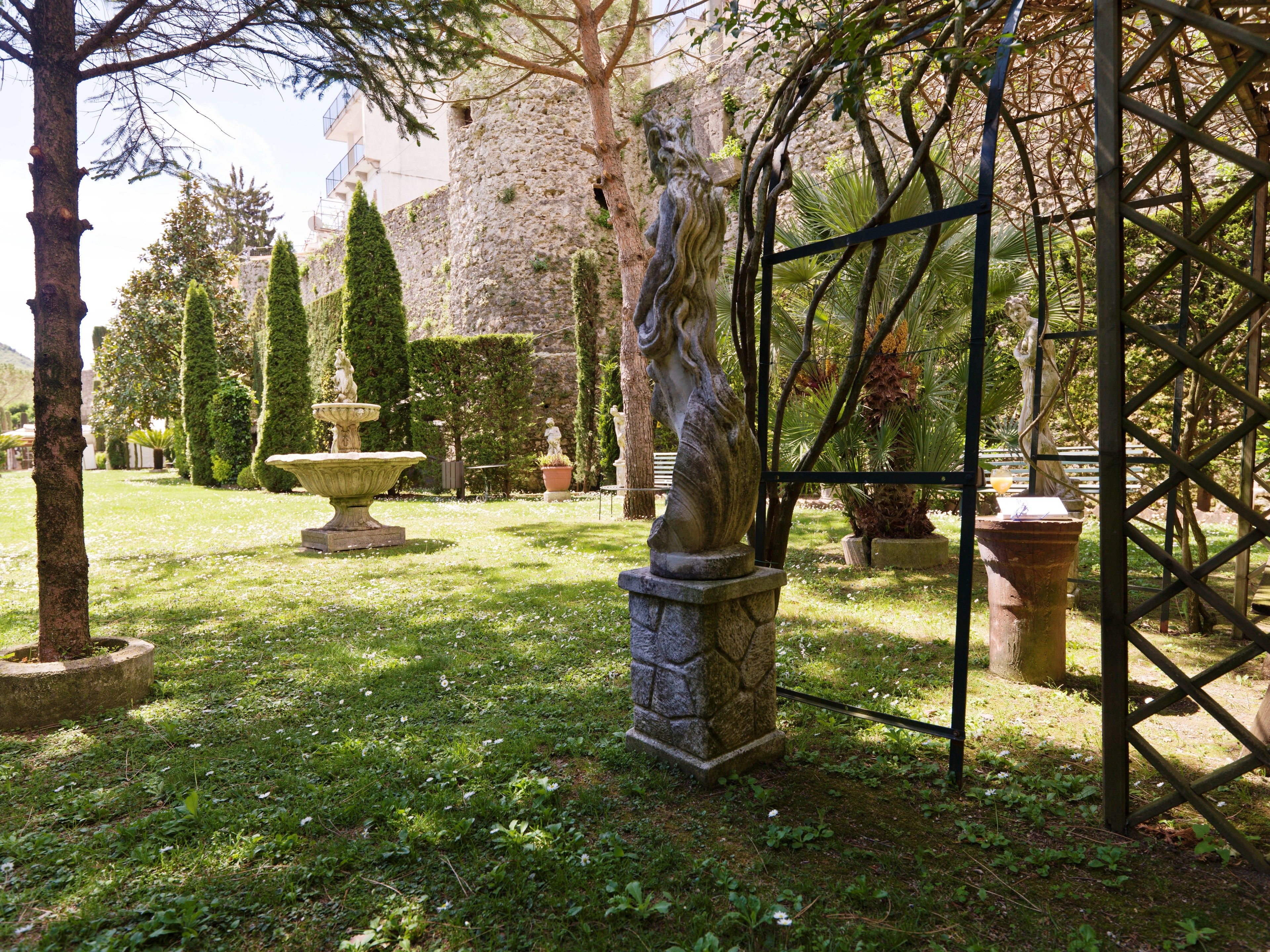 A garden with a statue, a fountain, and neatly trimmed hedges.