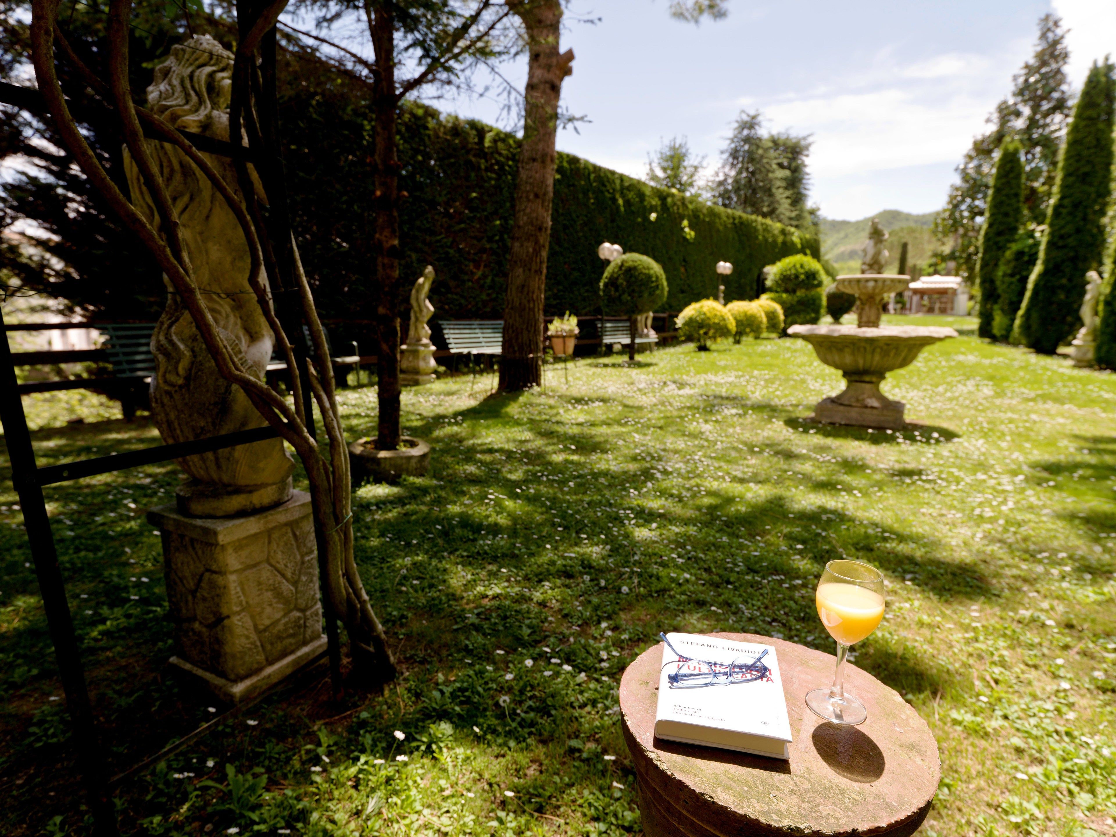 Ein Garten mit einer Statue, einer Bank und einem Buch auf einem Tisch, zusammen mit einem Glas Orangensaft.