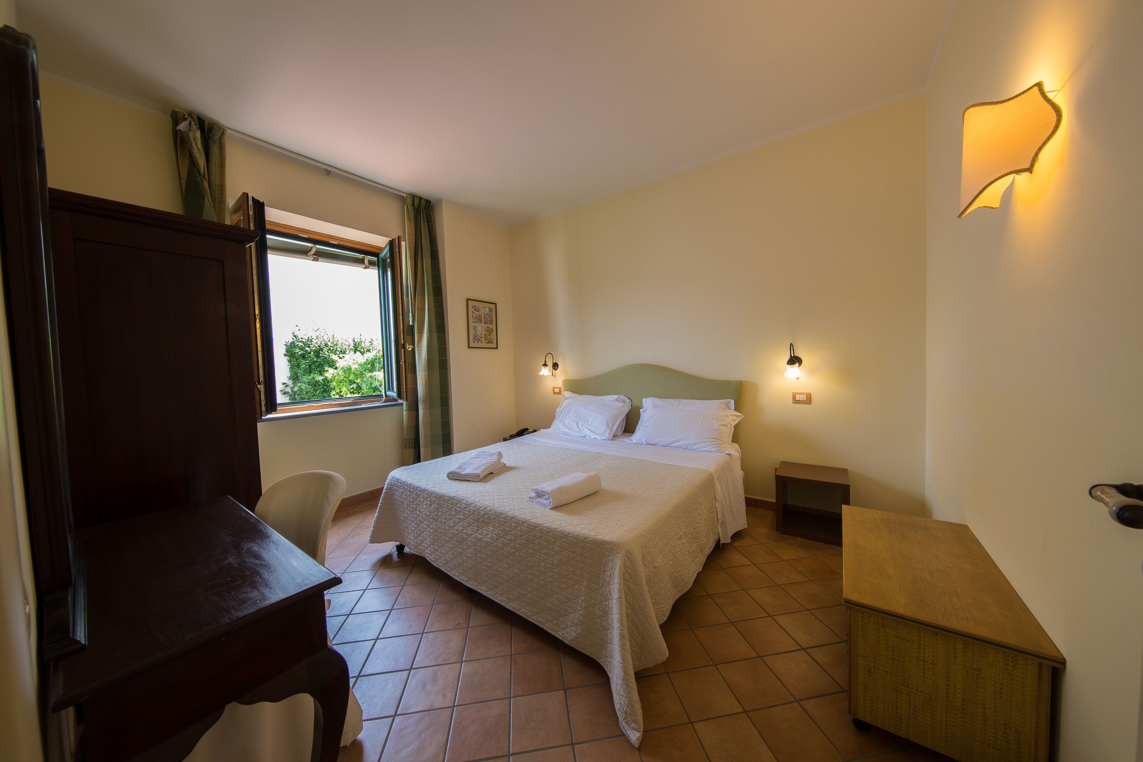 Une chambre d’hôtel avec un lit, des tables de chevet, un bureau et une fenêtre avec des rideaux.