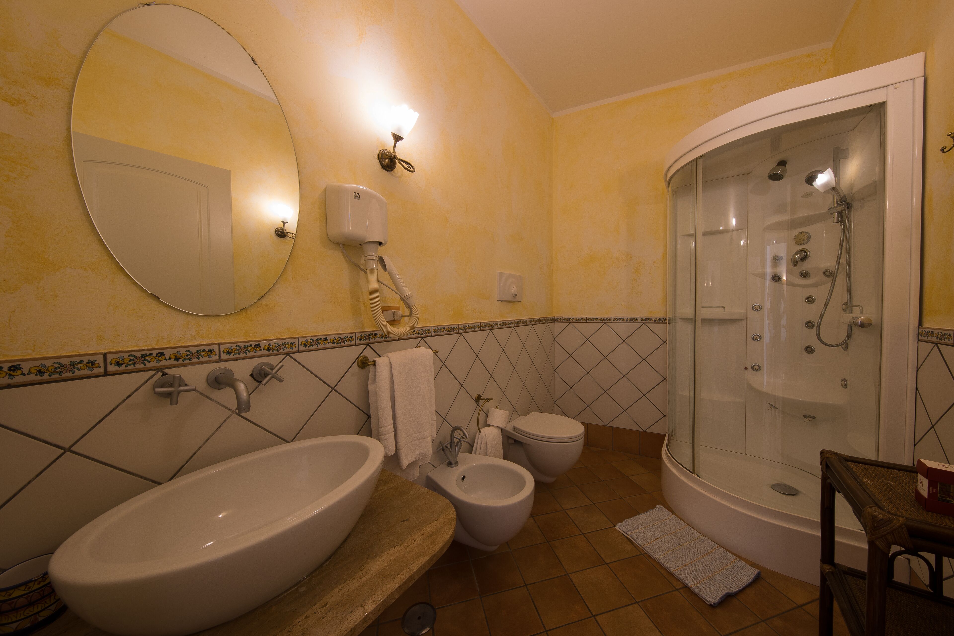Un baño con un lavamanos ovalado grande, un bidé, un inodoro y una cabina de ducha con paredes de vidrio.