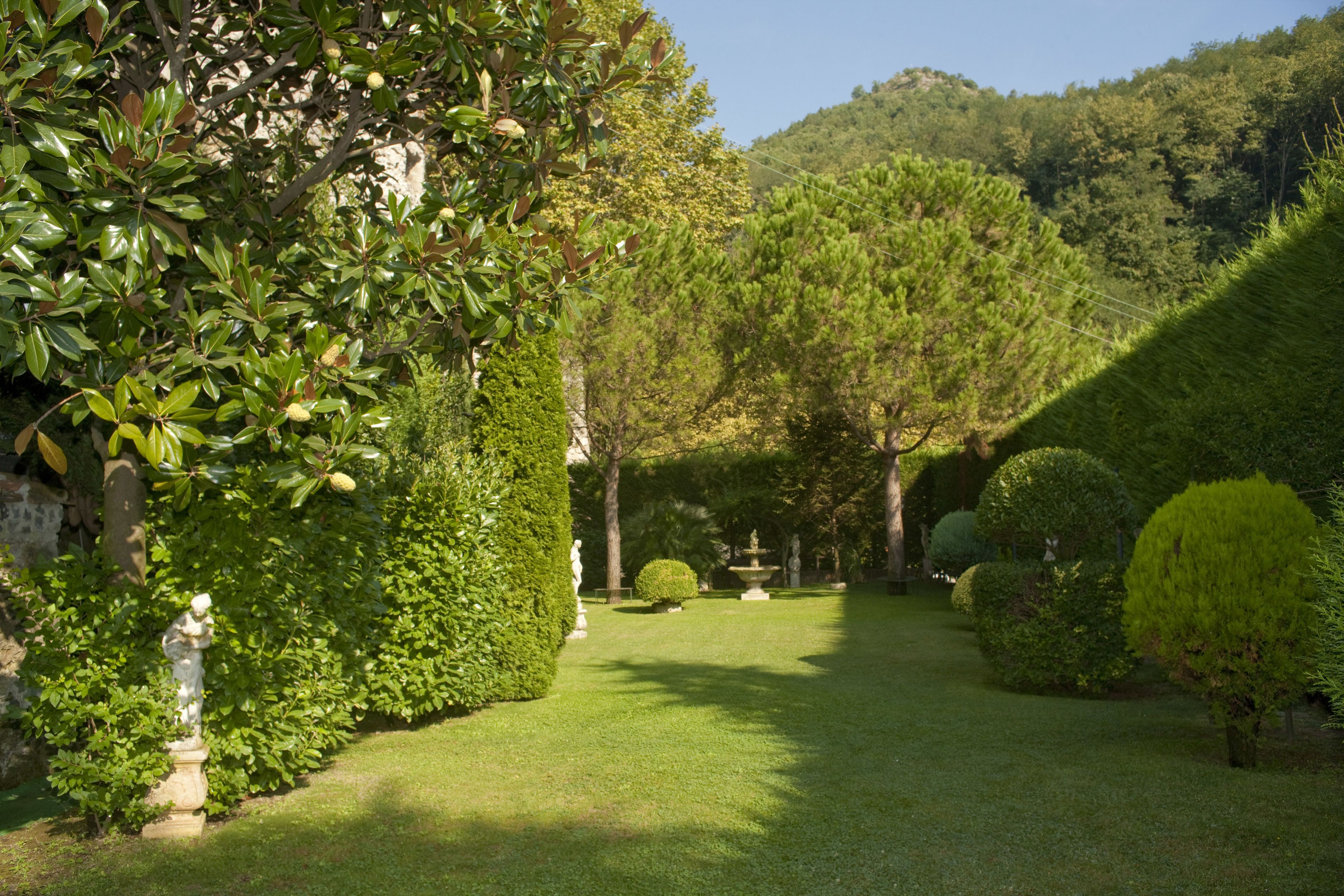 A well-maintained garden with manicured lawns, various shrubs, and a statue.