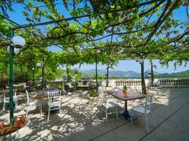 Un patio al aire libre con mesas y sillas, rodeado de follaje y vistas a montañas distantes.