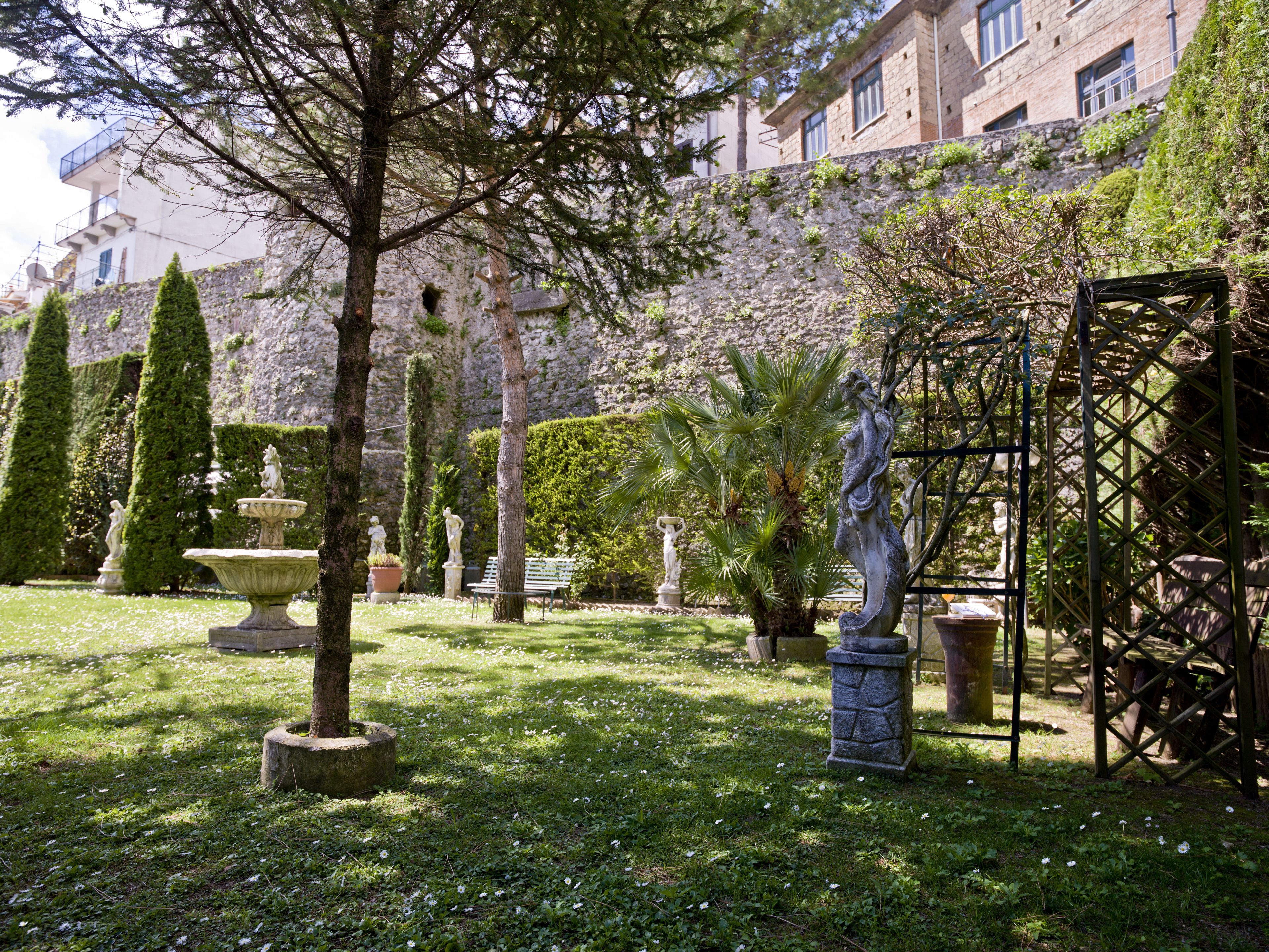A garden with statues, a fountain, and a building in the background.