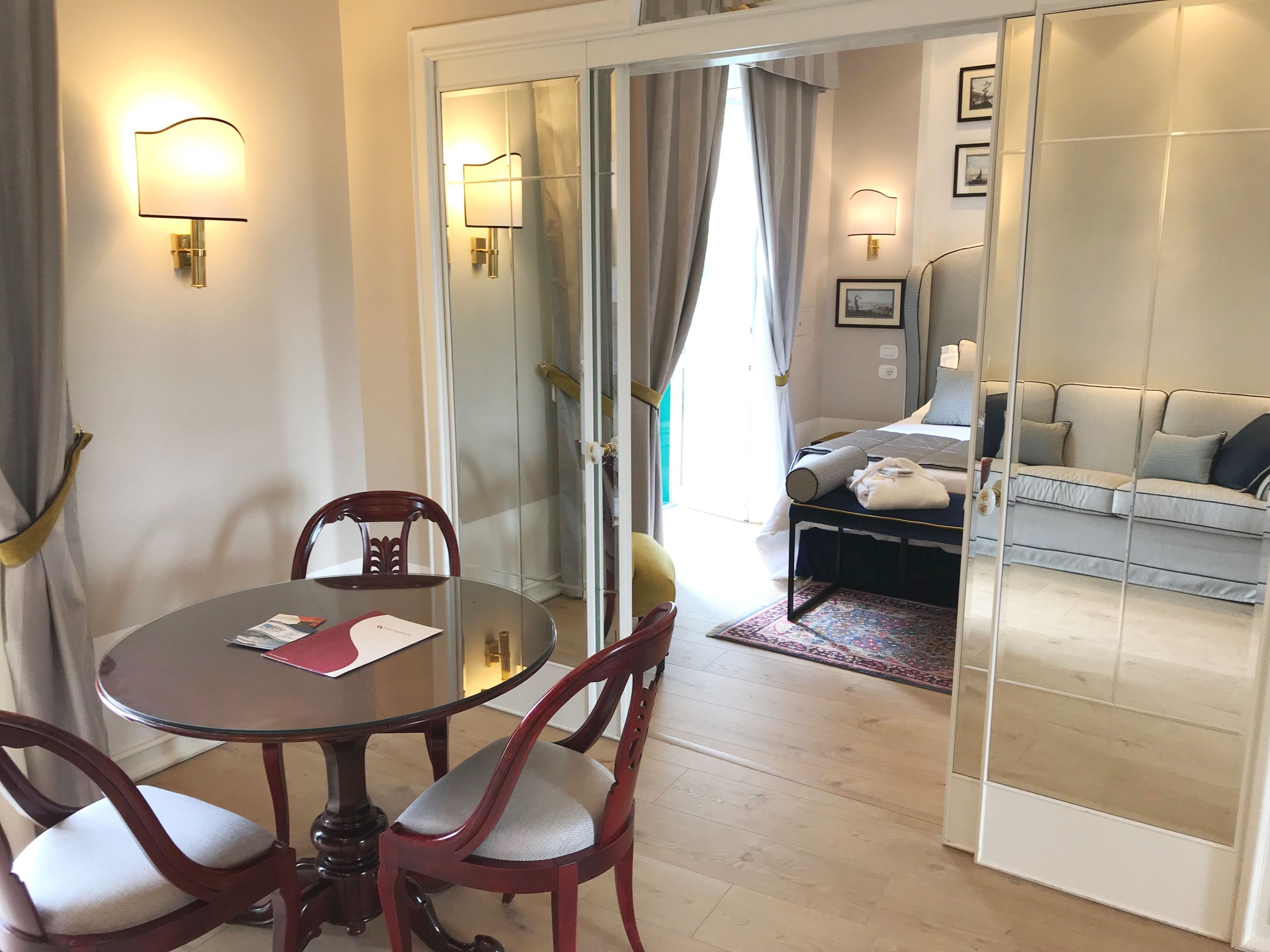 Quarto de hotel com área de refeições, incluindo uma mesa redonda, cadeiras, um sofá e um separador de vidro.
