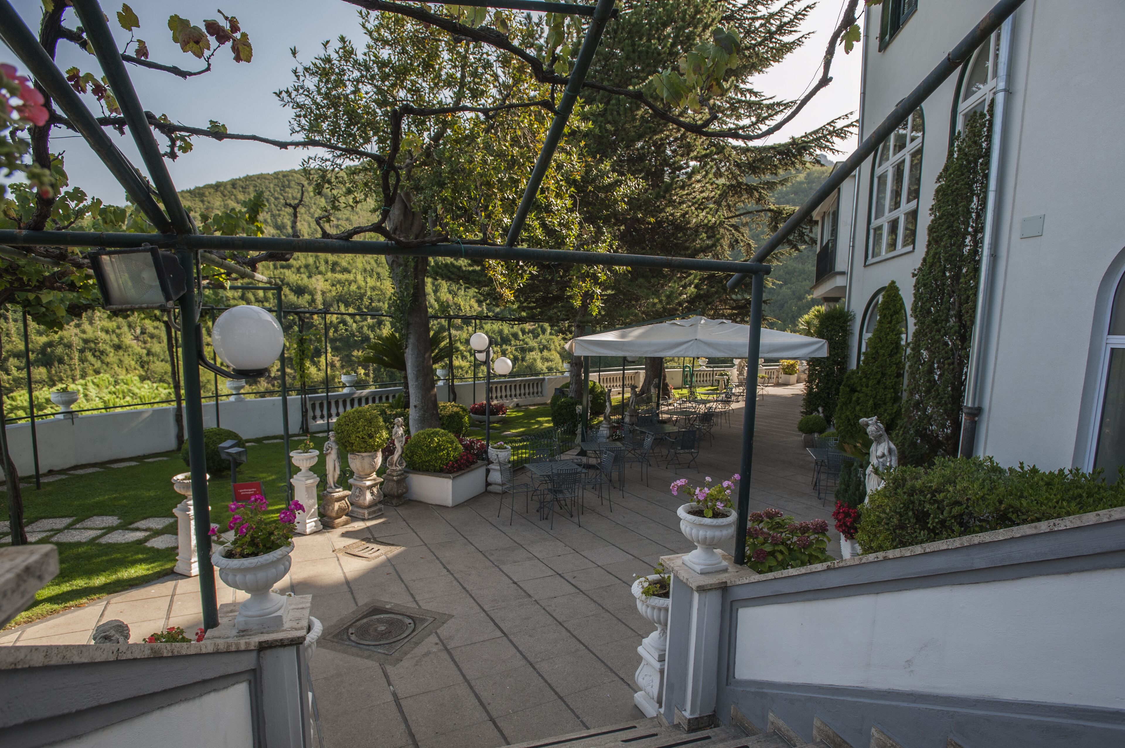 An outdoor patio area with tables and chairs, surrounded by potted plants and a white gazebo.