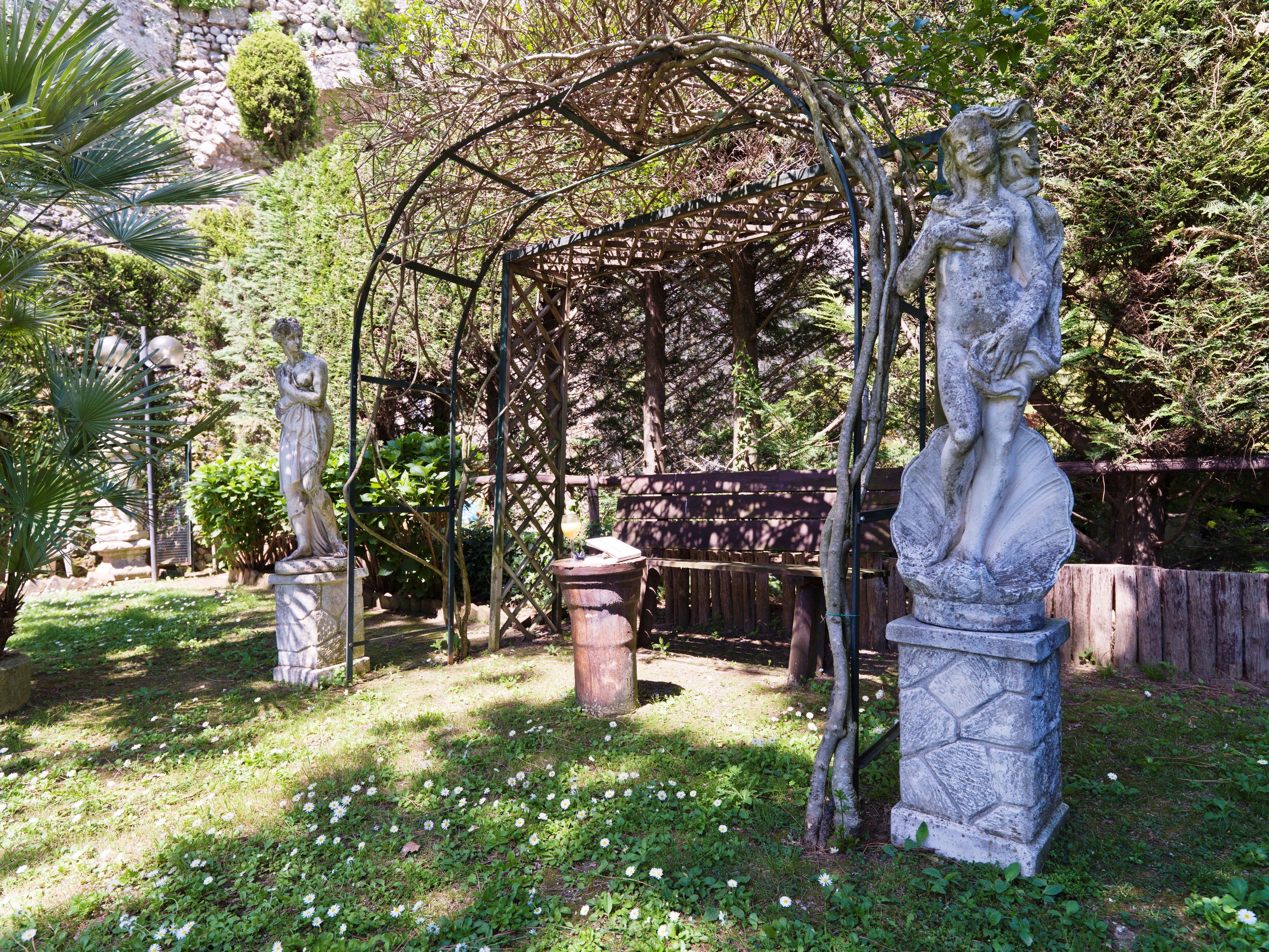 A garden with a statue, a pergola, and a wooden bench.
