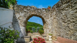 Un patio exterior con un arco de piedra, plantas en macetas, un banco y una mesa.