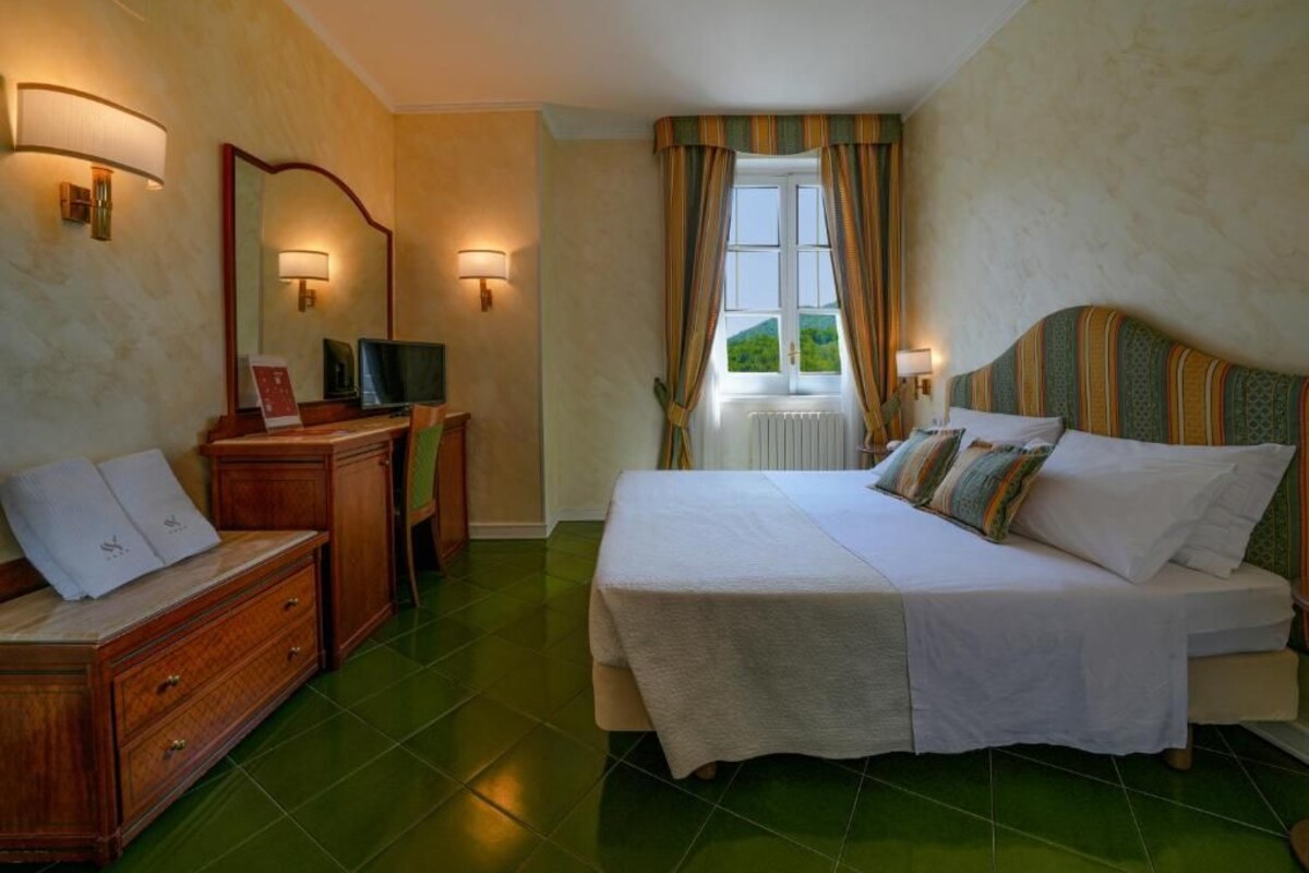 Habitación de hotel con cama, escritorio, espejo y ventana con cortinas.